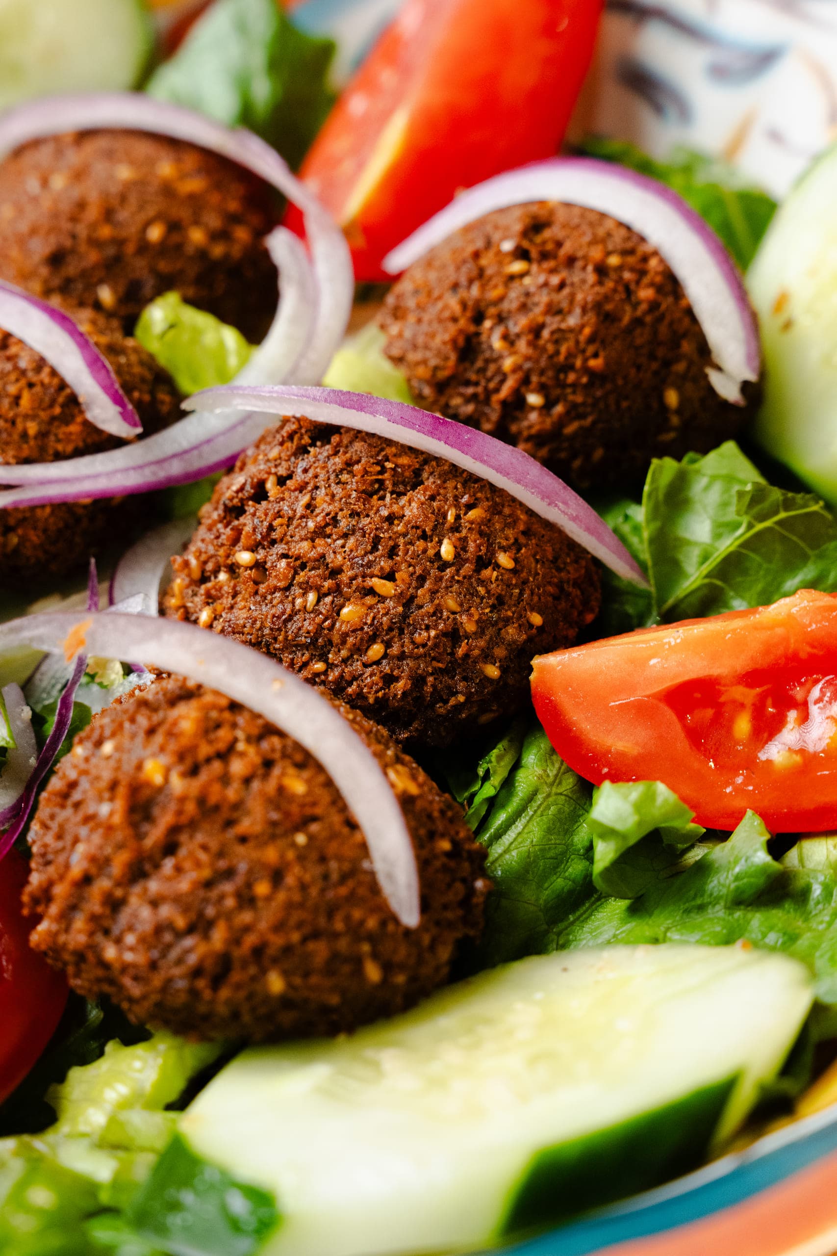Falafel over salad with red onion, tomato and cucumber