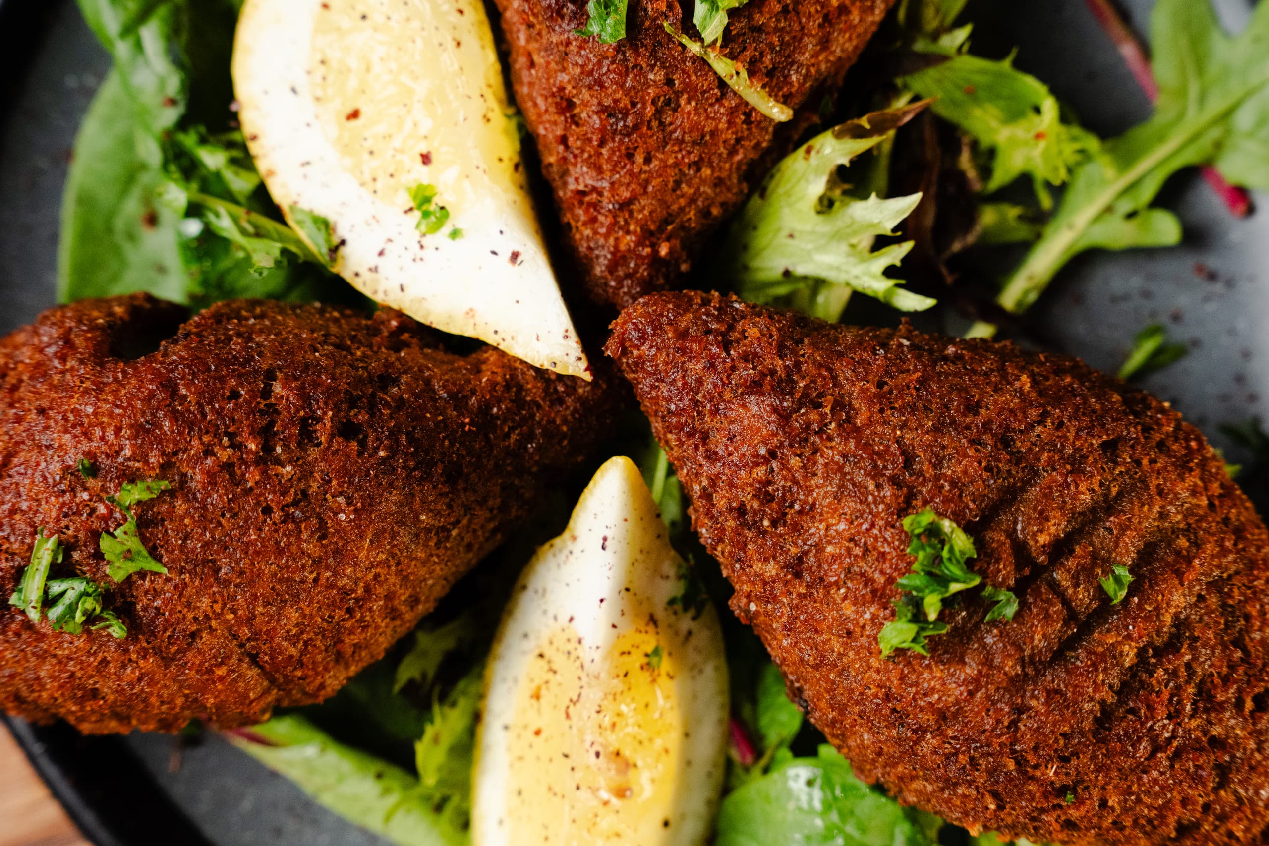 Kebbeh wedges plated with lemon and dressed leaves