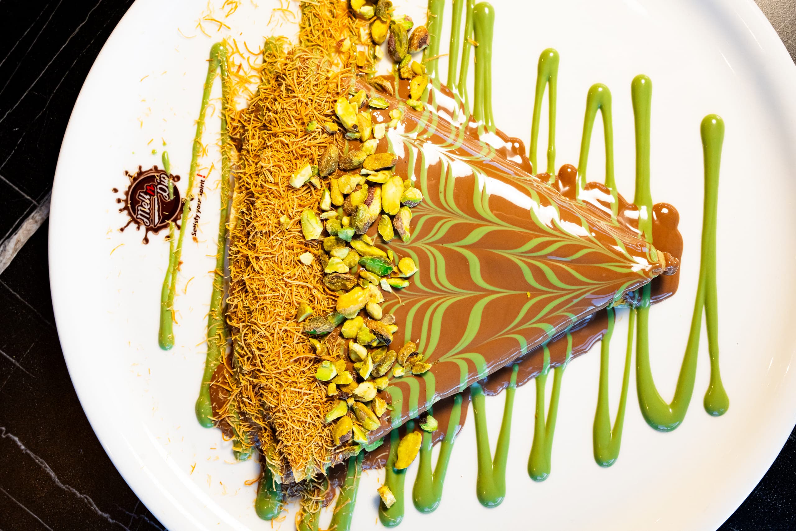 Pistachio dessert slice finished with crushed nuts and green sauce